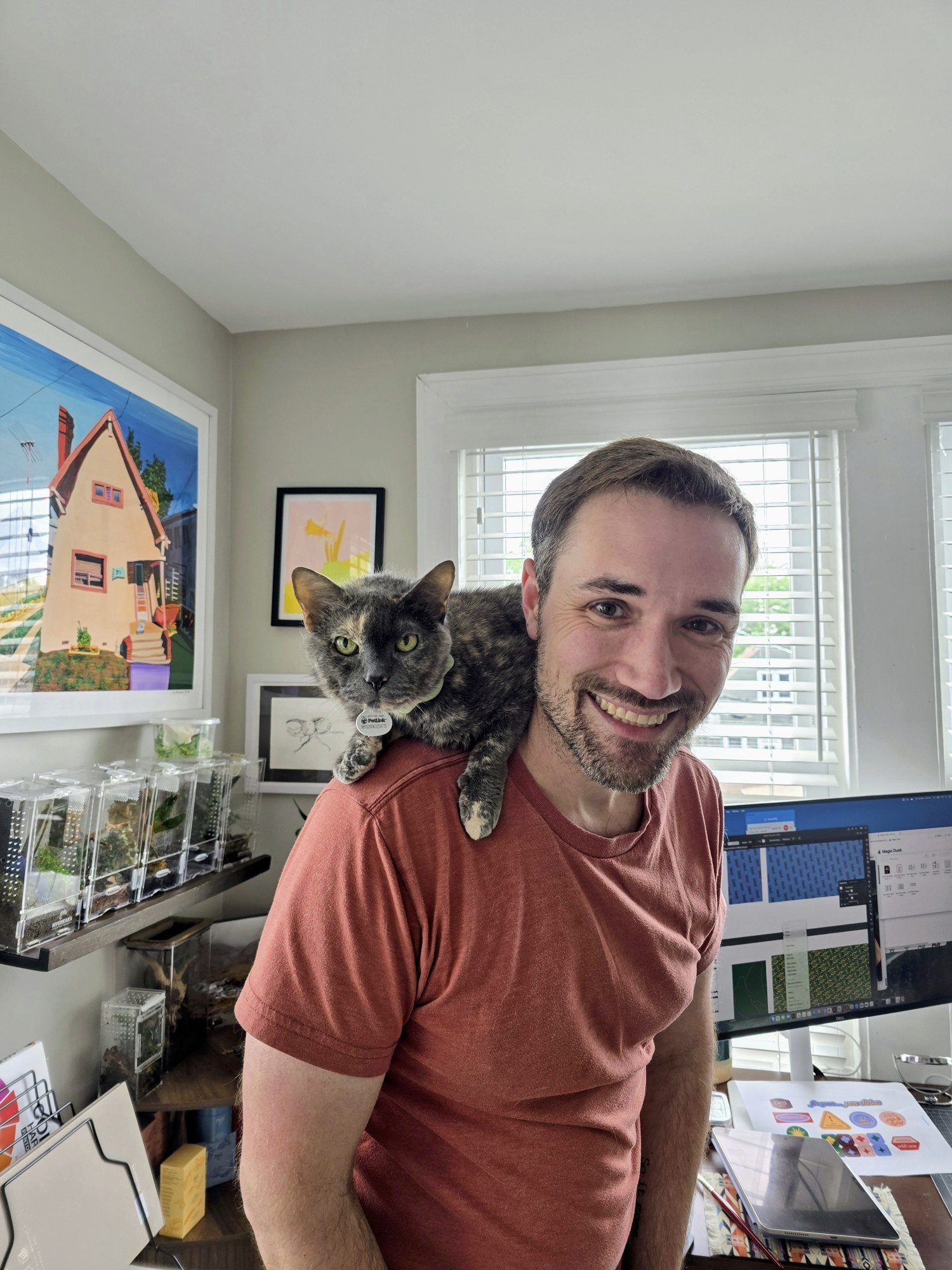 Doc Hazzard smiling in a home office, with a tortoiseshell cat resting on his shoulder